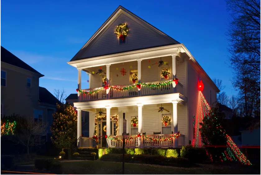 Two-story white house decorated with Christmas lights and wreaths, lit up at dusk.